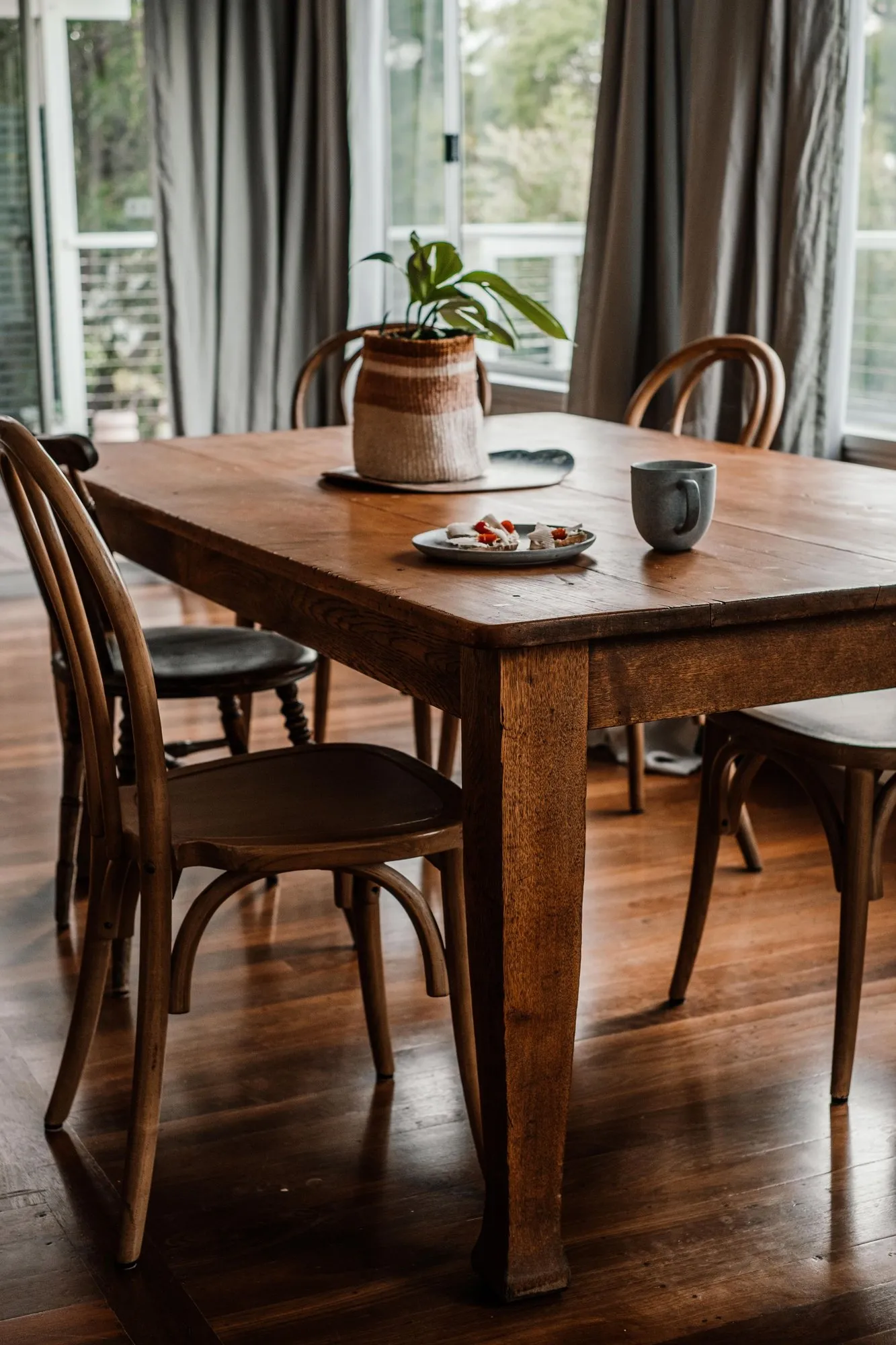 A wooden table by the window set with a plate and a mug of coffee