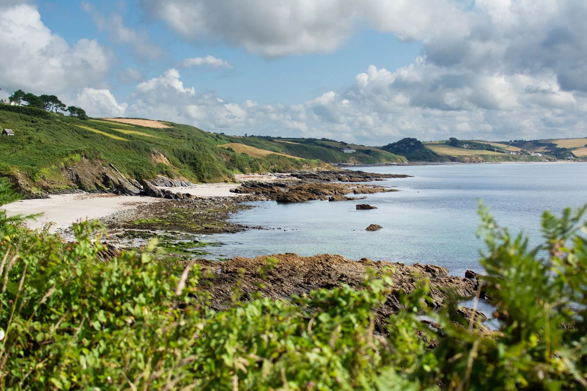 A curve of pale sand below wooded cliffs, with calm clear water